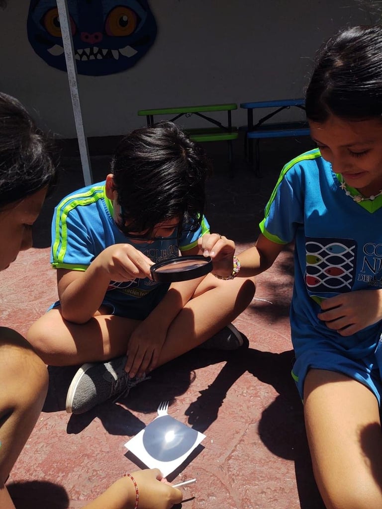 Children in blue and green sports shirts examining objects with magnifying glasses outdoors