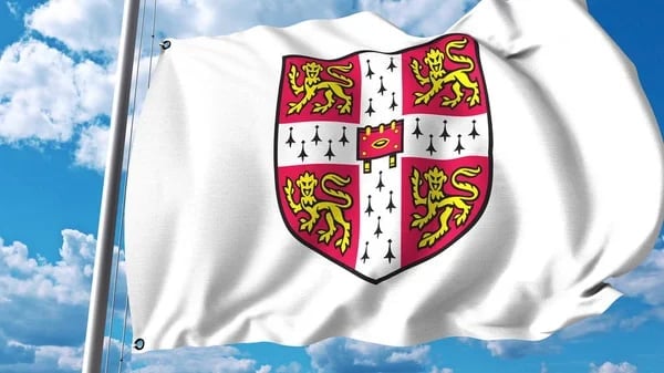 White flag with heraldic shield featuring red lions and fleur-de-lis symbols, waving against blue sky with clouds