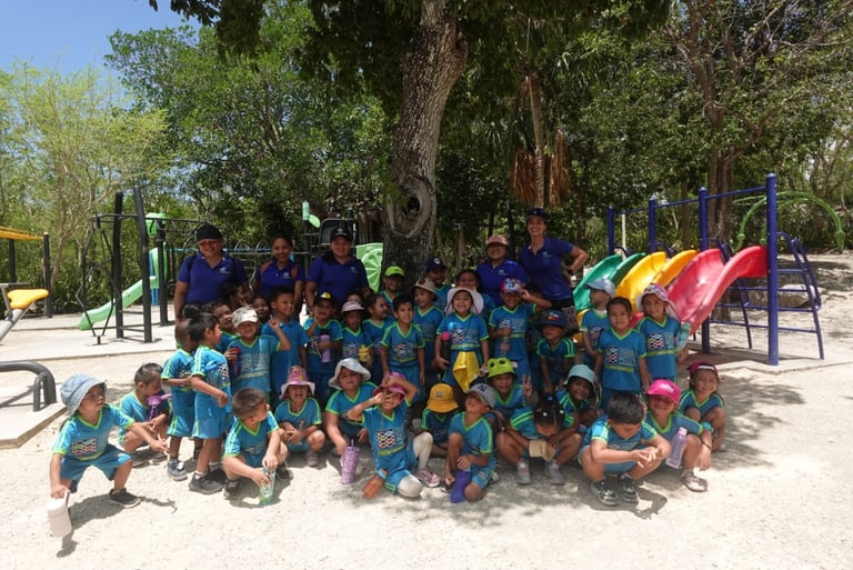 Large group of children and adults in matching blue shirts posing together at a playground with colorful slides and playground equipment