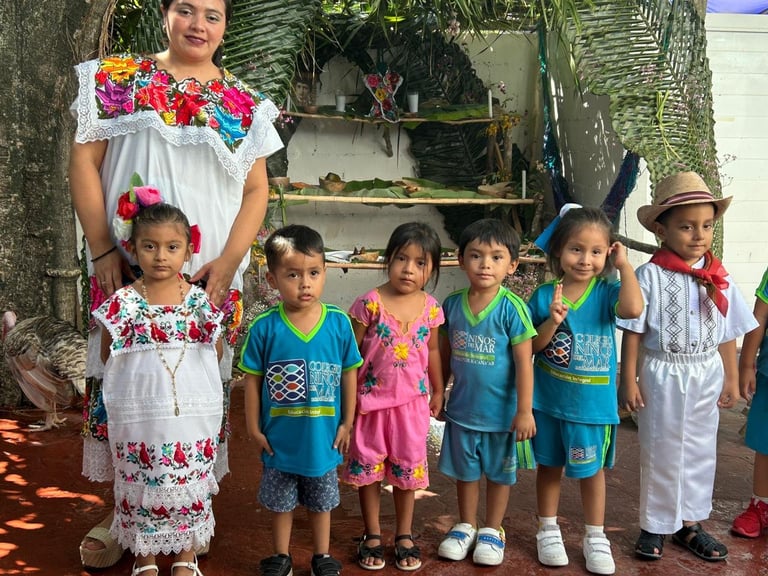 Woman and six children in colorful traditional and casual clothing standing together indoors with plants in background